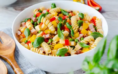 Bunter Nudelsalat ohne Mayo mit Spiralnudeln, Erbsen, Paprika und Schinkenwürfeln, garniert mit Basilikum.