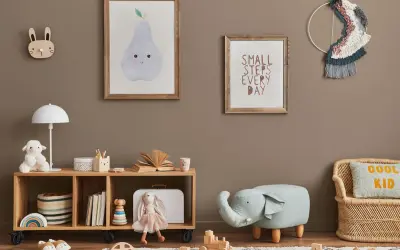 Przytulny pokój zabaw dla dzieci w domu. Na ścianie wiszą obrazki z gruszką i napisem "Small steps every day". Na półce stoi lampka, pluszowa owieczka i książki. Obok siedzi lalka-króliczek. Na podłodze leżą drewniane klocki i puf w kształcie słonia.