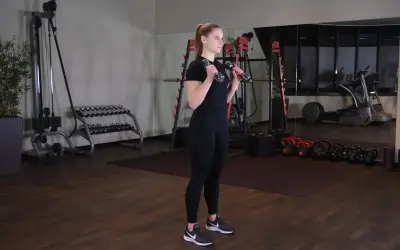 Kobieta wykonuje uginanie ramion z hantlami, ćwicząc bicepsy w siłowni.