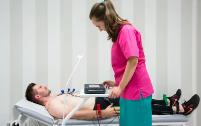 Pacjent leży na kozetce, pielęgniarka przygotowuje mu ekg spoczynkowe.