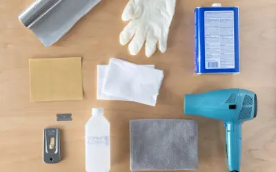 Kit pour savoir comment enlever du double face sur du carrelage : sèche-cheveux, grattoir, alcool isopropylique, gants, chiffons, papier de verre et rouleau d'aluminium.