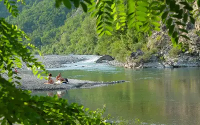 Un **lago vicino Milano con spiaggia** dove coppie si rilassano tra rocce e vegetazione lussureggiante.