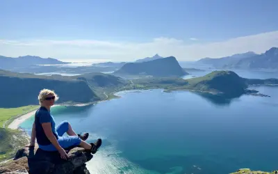 Kvinna sitter på klippavsats med fantastisk utsikt över fjordlandskap på Lofoten.