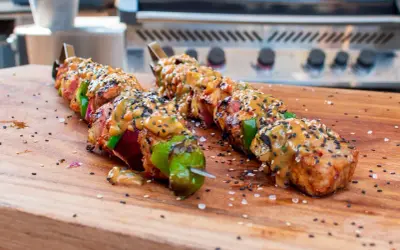 Fertige Schaschlik-Spieße mit Sauce und Sesam auf einem Holzbrett, bereit für den Schaschlik Grill.