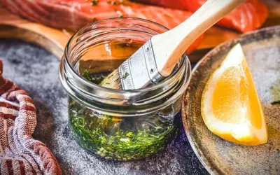 Marinade mit Kräutern und Zitrone bereit, um den Lachs zu verfeinern. Ein Pinsel liegt in der Glasflasche.