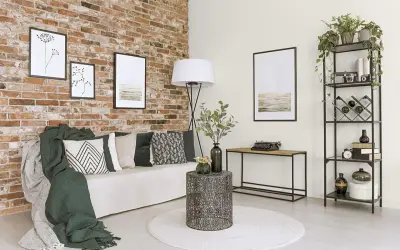 Nowoczesne ściany w salonie z cegły, ozdobione grafikami. Wygodna sofa z poduszkami i zielone narzuty tworzą przytulną atmosferę.