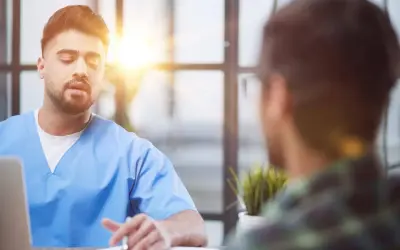 Lekarz w niebieskiej koszuli rozmawia z pacjentem. Czy trzeba mieć skierowanie do psychiatry? Zapytaj lekarza.