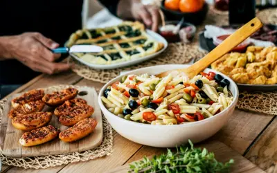 Pyszna sałatka makaronowa z oliwkami i pomidorkami, obok pieczywo i świeże oregano. Idealne na letni obiad, pokazujące co zrobić z oregano.