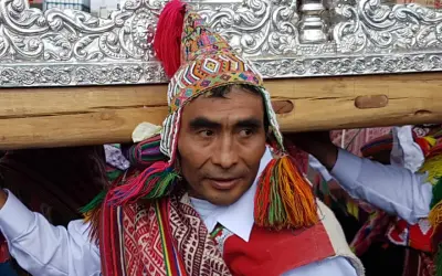 Kolorowy strój i tradycyjna czapka zdobią jednego z mężczyzn niosących ozdobną ramę. To **Indianie z Cuzco** podczas uroczystości.