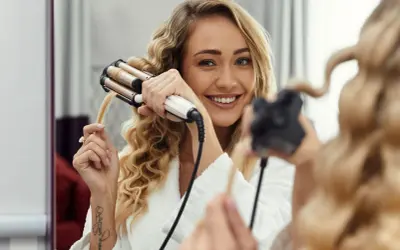 Uśmiechnięta blondynka tworzy sobie fale hollywoodzkie za pomocą lokówki.