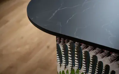 Plan de travail de cuisine en marbre noir avec un motif de plumes colorées sur le côté, créant une profondeur visuelle.