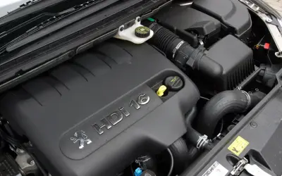 Silnik 2.0 HDI pod czarną osłoną z logo Peugeot. Widać przewody, filtr powietrza i zbiorniczek płynu.