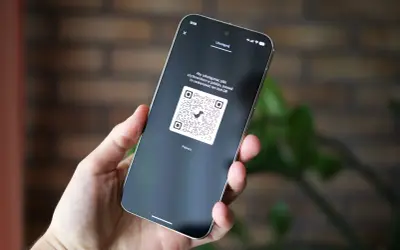 Dłoń trzyma smartfon z wyświetlonym kodem QR, który można zeskanować, aby udostępnić pliki.
