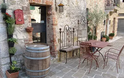 Un angolo pittoresco nella regione del Chianti con un barile di legno, piante aromatiche, un tavolino da esterno e un vecchio cancello in ferro battuto.