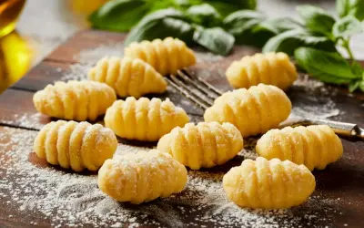 Świeżo przygotowane, puszyste makaron gnocchi, posypane mąką, leżą na drewnianej desce obok gałązek bazylii.