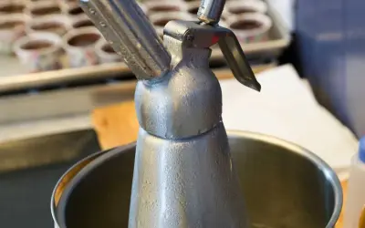 Metalowy syfon do bitej śmietany, pokryty kroplami kondensatu. Zastanawiasz się, ile może stać w lodówce?