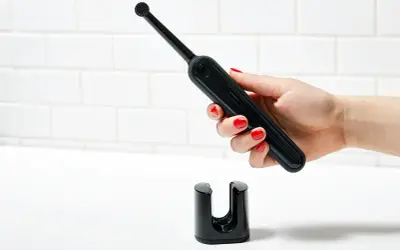 Mano con smalto rosso tiene uno spazzolino elettrico nero sopra il suo supporto. Un modo efficace per pulire muffa spazzolino elettrico.