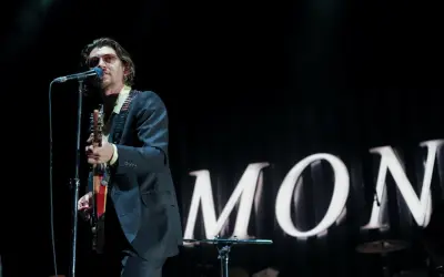 Alex Turner w okularach przeciwsłonecznych śpiewa i gra na gitarze podczas jednego z koncertów Arctic Monkeys.