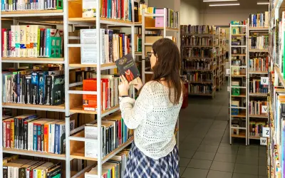 W bibliotece, gdzie **miejscu możecie znaleźć szeroki** wybór książek, młoda kobieta przegląda półki, trzymając w ręku jedną z pozycji.