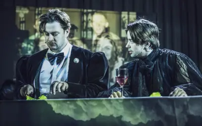 Dwóch mężczyzn przy stole, jeden w czarnym aksamicie, drugi w koronkowej szacie. Może to Hamlet i Ofelia?