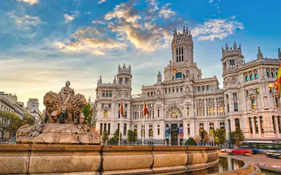 Cibelesfontänen framför det ståtliga Palacio de Comunicaciones, ett ikoniskt konstmuseum i Madrid, under en dramatisk solnedgång.