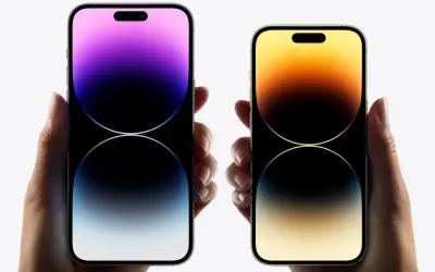 Dwie dłonie trzymają telefony iPhone 16. Jeden z nich ma fioletowy ekran, drugi złoty.
