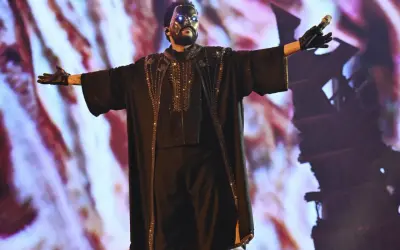 The Weeknd w masce i błyszczącym stroju na koncercie w Polsce, z rękami rozłożonymi szeroko.