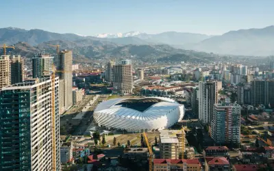 Widok na nowoczesne miasto z futurystycznym stadionem i górami w tle. Rozwój infrastruktury, budowa nowych wieżowców. Batumi ceny nieruchomości mogą być tu atrakcyjne.