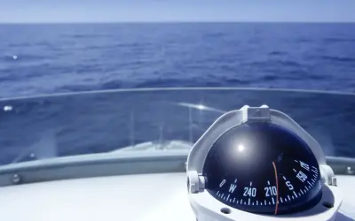 Kompass auf einem Boot zeigt die Richtung auf dem Meer. Teile des Bootes wie das Deck und die Windschutzscheibe sind sichtbar.