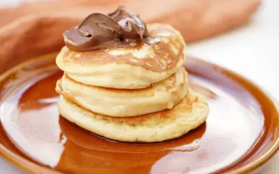En hög med fluffiga american pancakes toppas med chokladkräm på en brun tallrik.