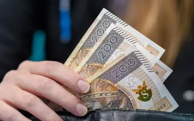 Dłoń trzyma banknoty 200 zł. Może to symbolizować wsparcie finansowe, np. stały zasiłek dla bezrobotnych po 50 roku życia.
