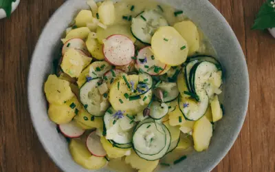 Kartoffelsalat mit Schale, garniert mit Radieschen, Gurken und Schnittlauch. Ein herzhaftes Gericht, das an Omas Küche erinnert.