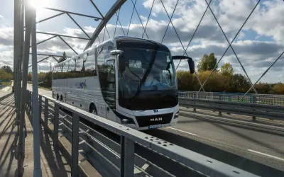 Autobus PKS NOVA na moście, podróżujący z Grajewa do Augustowa. Słoneczny dzień, chmury na niebie.