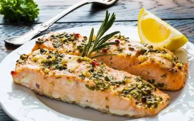 Delizioso salmone al forno con erbe aromatiche, aglio e peperoncino, guarnito con rosmarino e una fetta di limone.