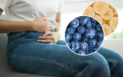 Osoba z bólem brzucha trzyma się za żołądek. Obok zdjęcia jagód i plasterków banana, które mogą pomóc na biegunkę.
