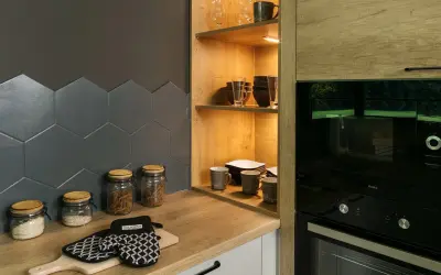 Drewniane półki do kuchni z naczyniami i słoikami z produktami. Obok piekarnik i mikrofalówka.