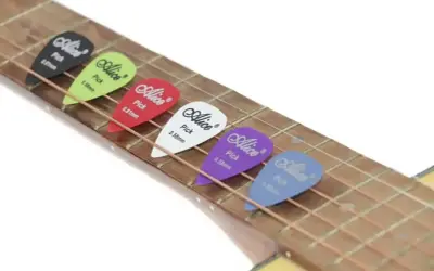 Kolorowe kostki do gry na gitarze Alice leżą na strunach. Każda kostka ma inny kolor i grubość, gotowa do tworzenia muzyki.