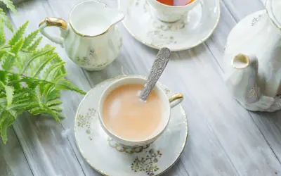 Elegancka filiżanka z herbatą z mlekiem, ozdobiona złotymi wzorami, obok dzbanuszka i czajniczka.