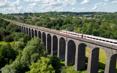 Ett modernt tåg susar fram över en gammal tegelbro, en perfekt bild för att tågluffa i England.