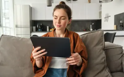 Kobieta na kanapie przegląda tablet, być może szukając informacji o kursach fakultatywnych.