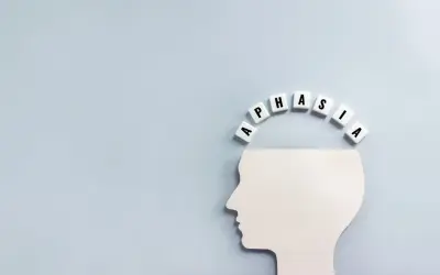 Biały profil głowy z literami tworzącymi słowo "APHASIA" nad nim. Obraz symbolizuje, co to jest afazja – trudności z mową i rozumieniem.