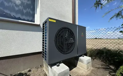 Nowoczesna pompa ciepła Geo Power, która obniża koszt ogrzewania domu. Urządzenie stoi na betonowych bloczkach przy ścianie budynku.