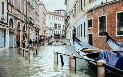 Venecia cuando se inunda: góndolas esperan en canales crecidos, peatones cruzan un puente sobre el agua que llega a las puertas de las tiendas.