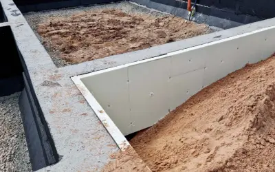 Budowa domu w toku: betonowe stopy fundamentowe, izolacja ze styropianu i nasypy ziemi.
