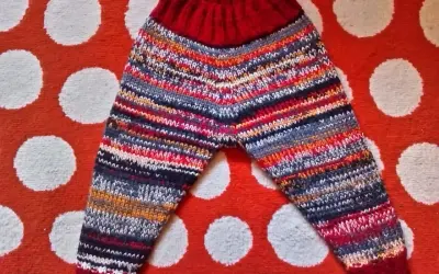 Pantalón de punto para bebé con rayas multicolores y cintura roja, sobre fondo de lunares.