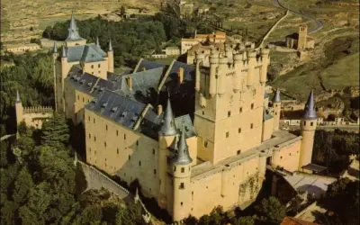 Vista aérea del Alcázar de Segovia, con sus torres y tejados, rodeado de vegetación. La sala de los reyes se intuye en su imponente estructura.