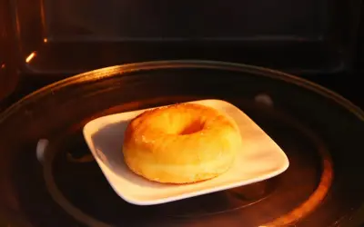 Ein einzelner Donut auf einem weißen Teller in einem Mikrowellenofen. So bleiben Donuts frisch.