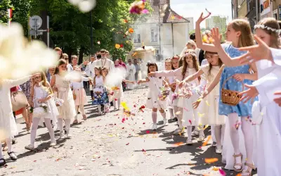 15 czerwca. Dzieci w białych strojach sypią kwiaty podczas procesji. W tle widać duchownych i wiernych.
