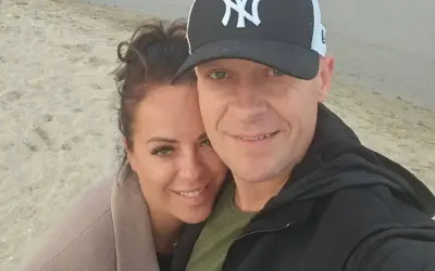 Piotr Marciniak z żoną na plaży, uśmiechnięci i blisko siebie.