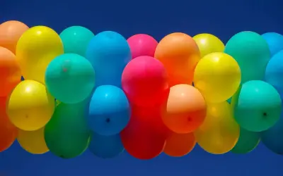 Un amas de ballons colorés flottant dans un ciel bleu. Combien de temps tient un ballon gonflé à l'air ? Cela dépend de sa taille et du matériau.
